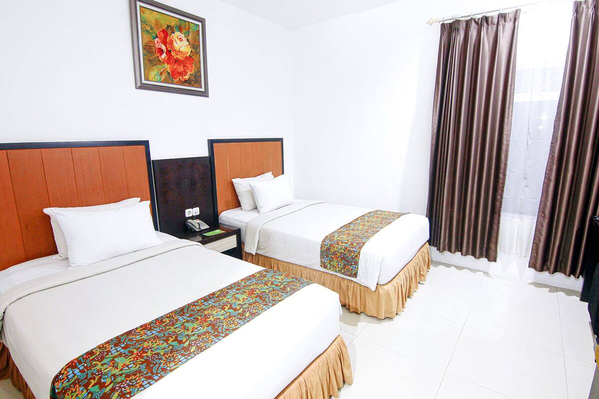 A hotel room with two beds, a painting on the wall, and a window with curtains.