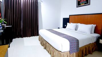 Habitación de hotel con una cama grande, cabecera de madera, mesita de noche, escritorio con planta y ventana con cortinas.