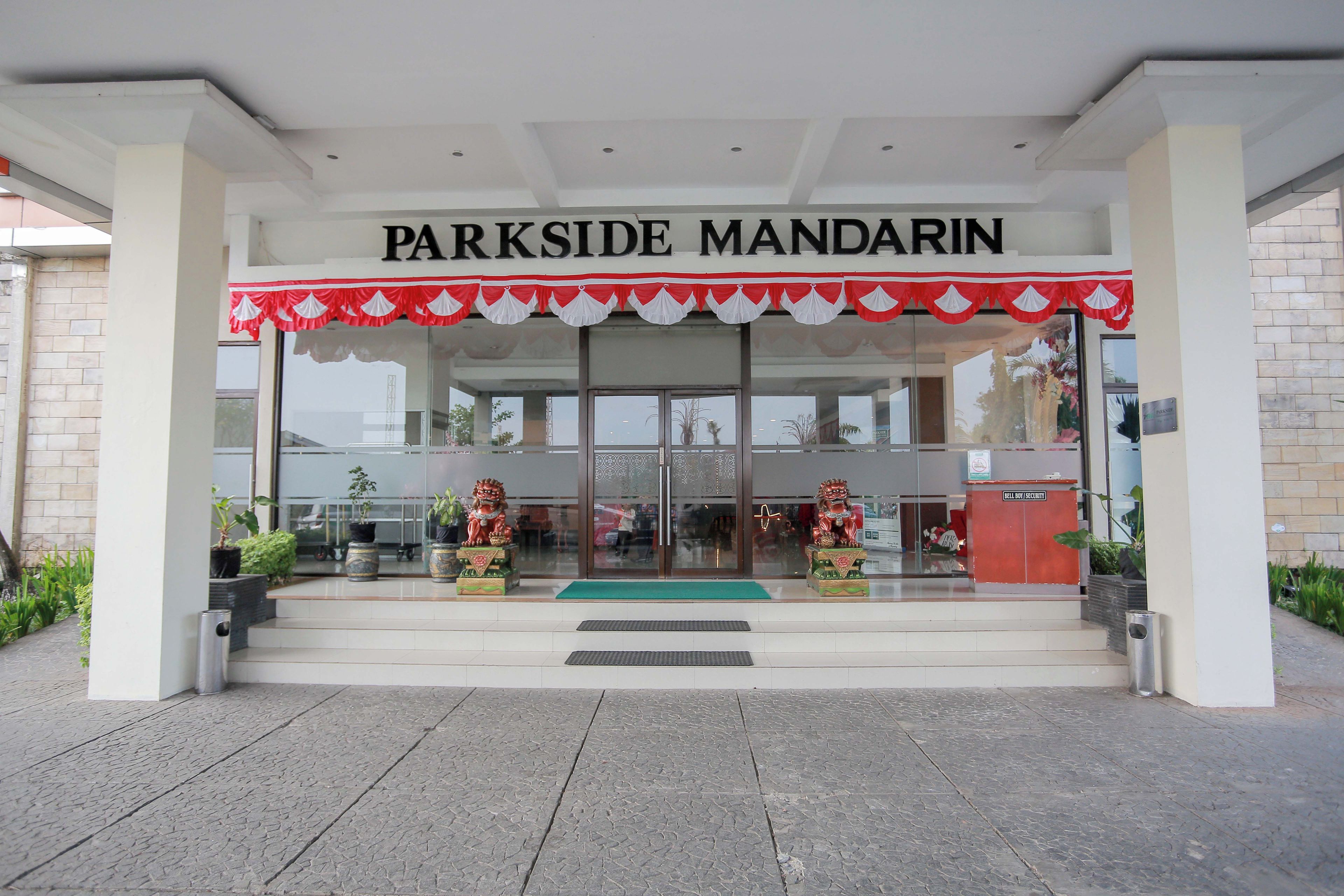 L’entrée de Parkside Mandarin se distingue par son auvent rouge et blanc, un poste de sécurité et des plantes en pot.