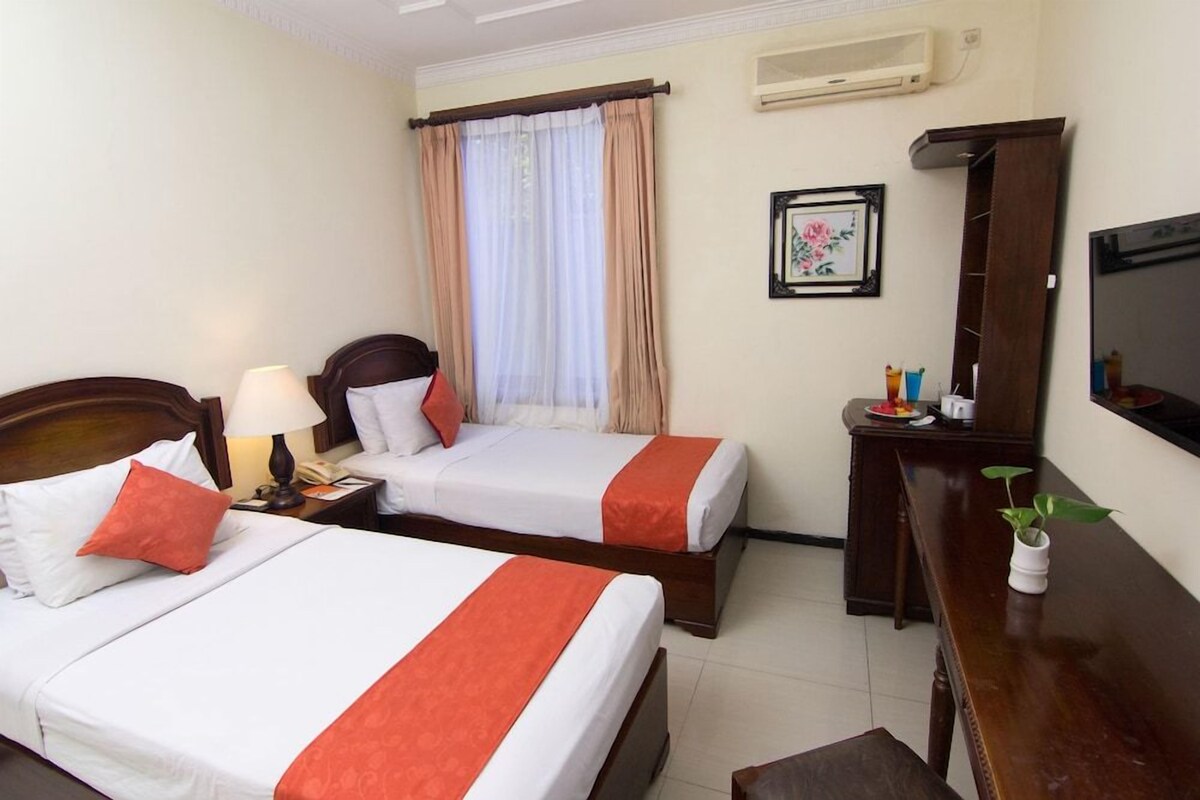 A hotel room with two beds, a desk, a TV, and a window with curtains.