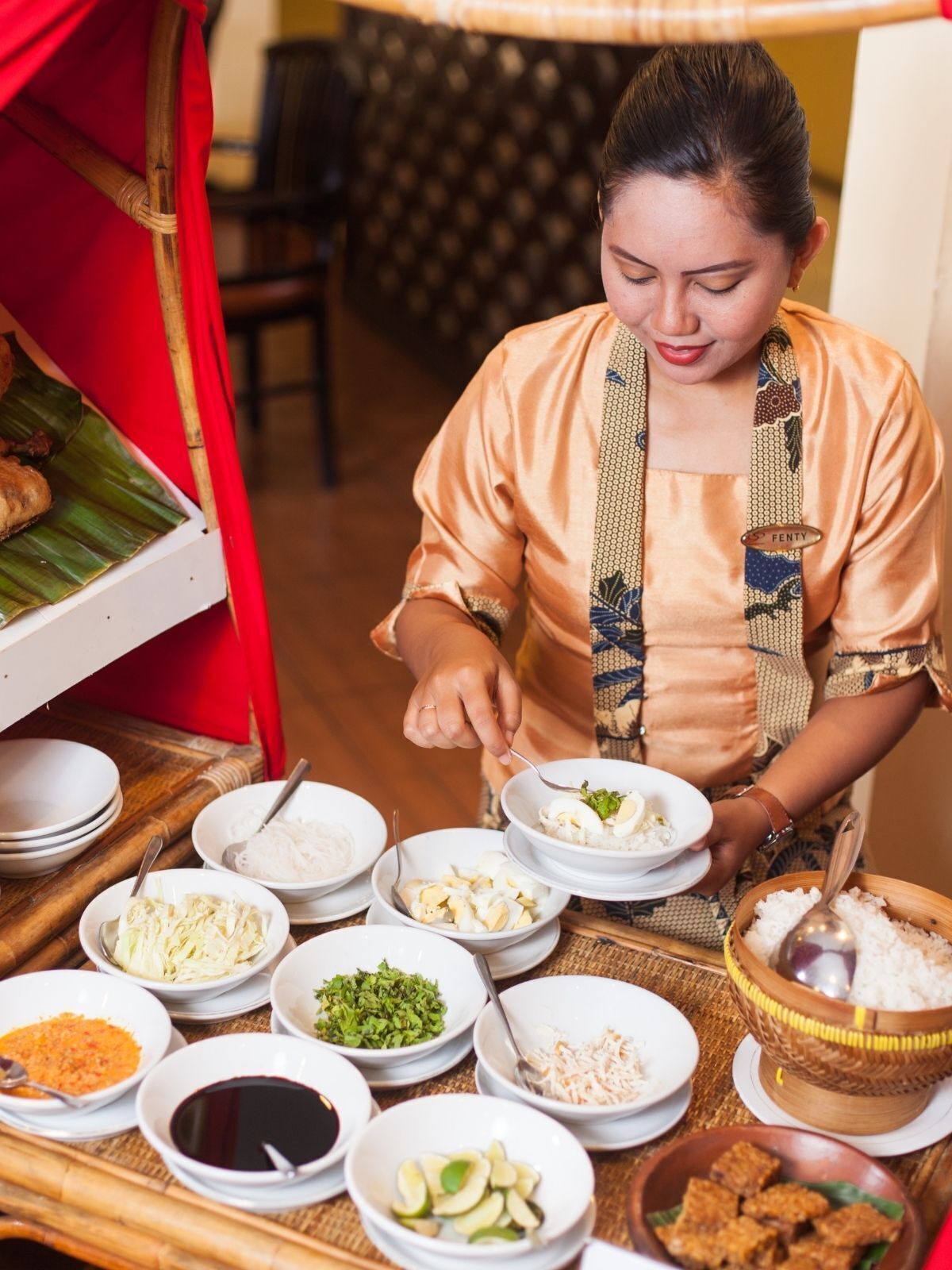 A person serving food from a variety of bowls on a table, including rice, vegetables, and a dish with meat.