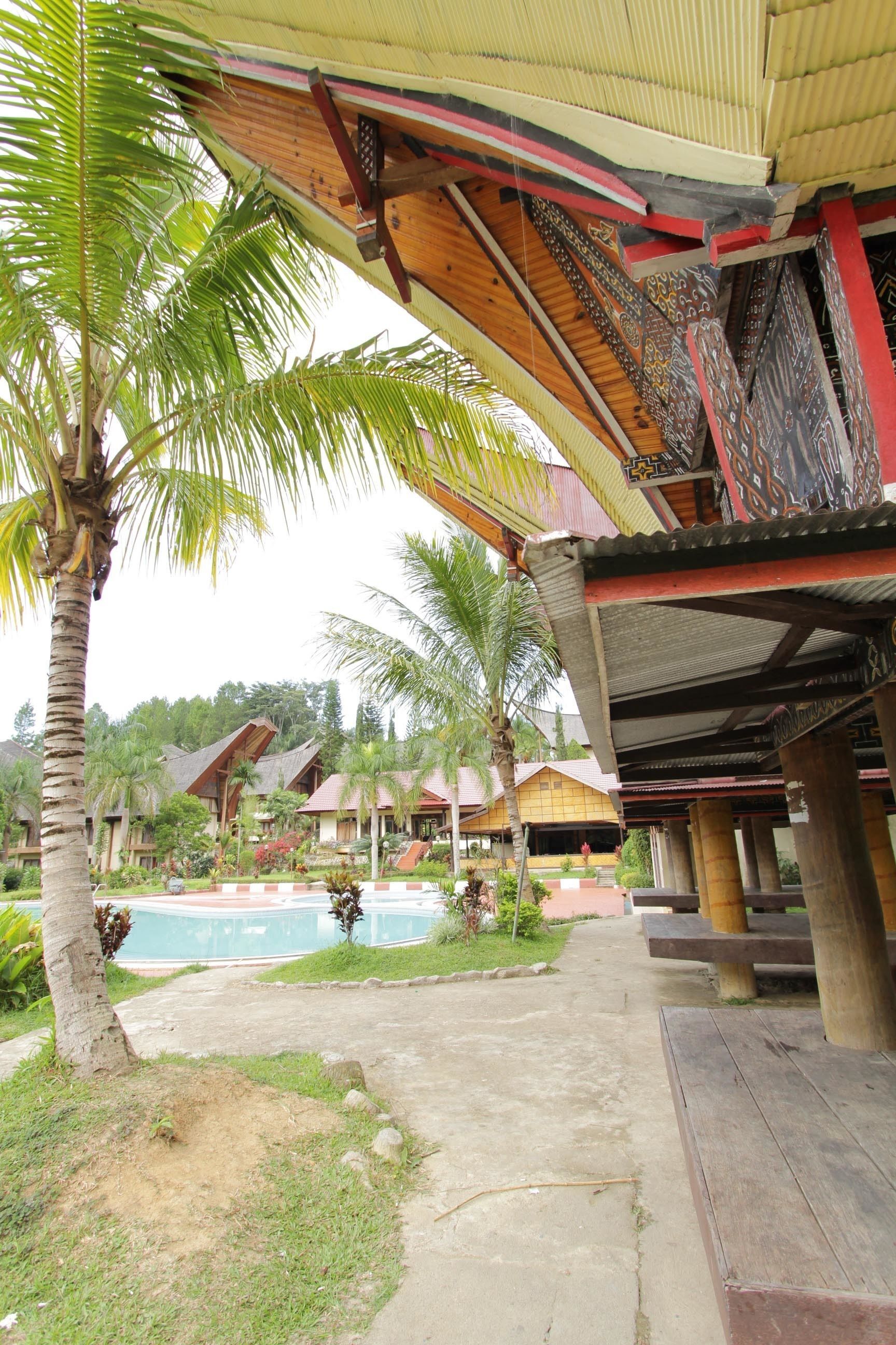 A resort with a pool, palm trees, and traditional wooden architecture.
