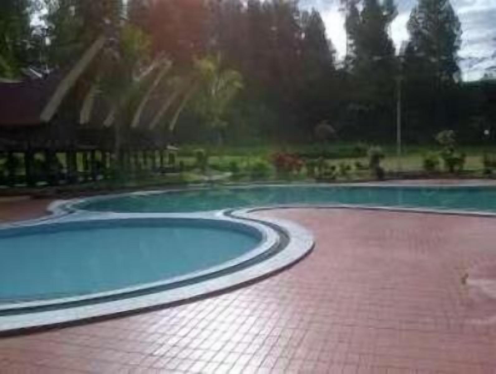A swimming pool with a curved edge, surrounded by a paved area and a covered structure.