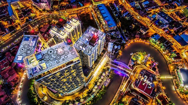 Vista aérea de una zona urbana moderna con edificios iluminados, un río y una vía circular.
