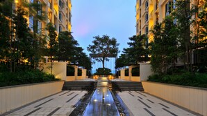 Un sendero bien iluminado que conduce a la entrada de un edificio, bordeado por árboles y una fuente de agua.