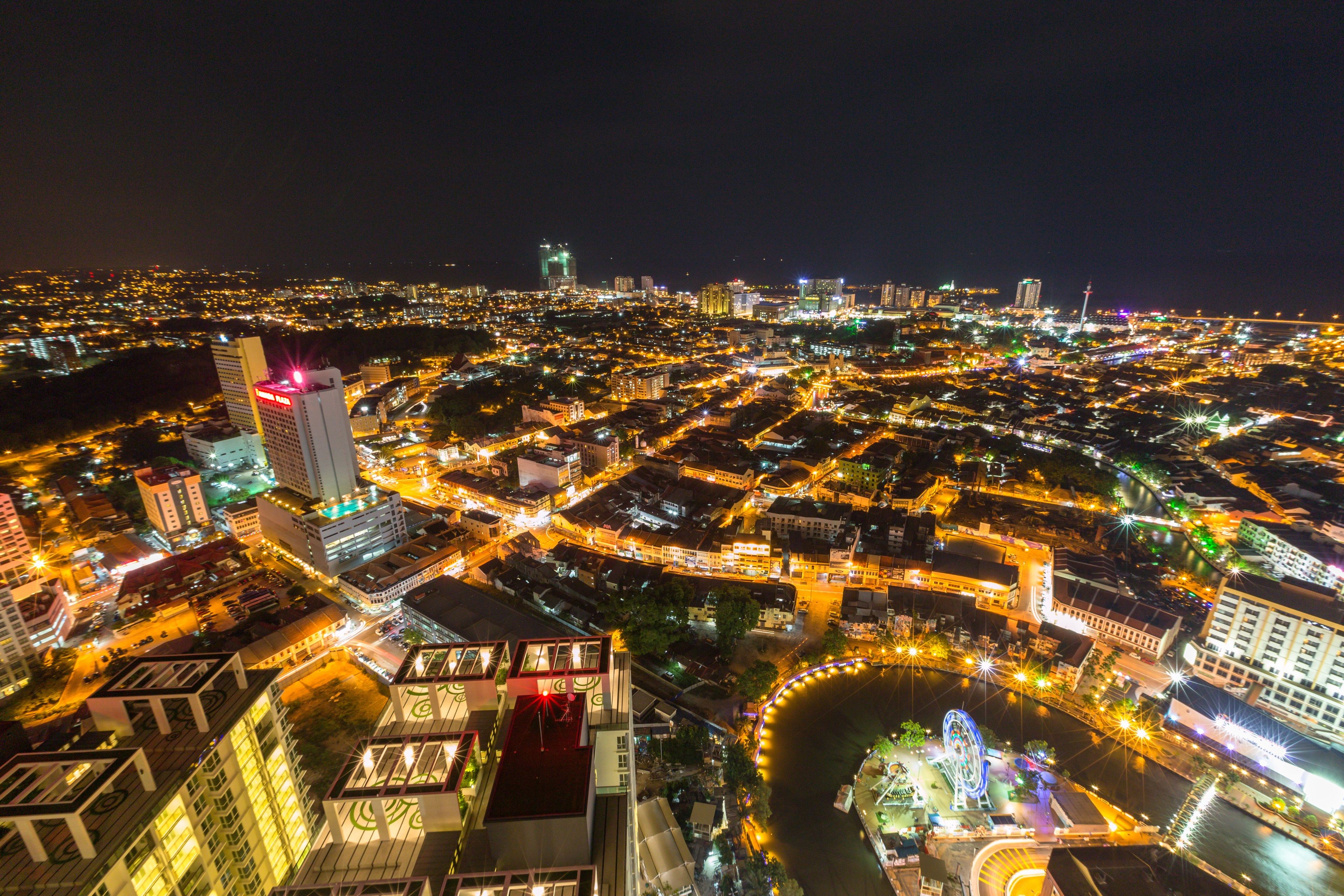Une vue aérienne nocturne d’une ville, avec ses bâtiments illuminés, une rivière et une grande roue.