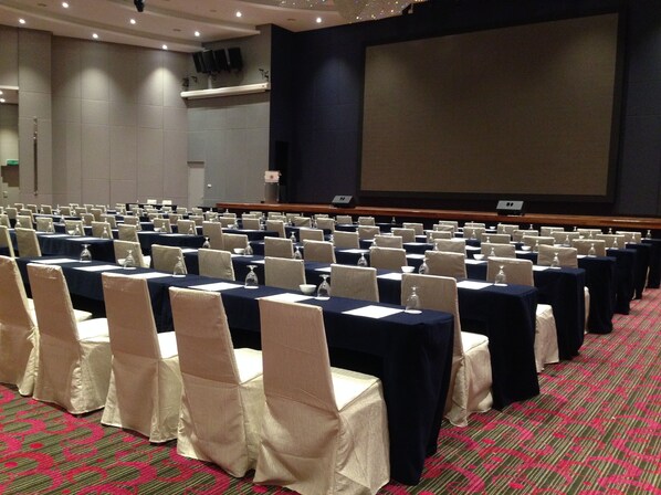 A conference room with rows of tables and chairs, a large screen, and a carpeted floor.