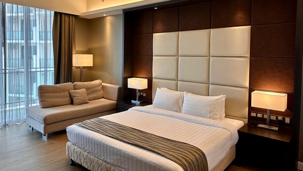 A modern hotel room with a large bed, a sofa, two bedside lamps, and a view of the city through large windows. - Swiss-Garden Hotel Melaka (Malacca City)
