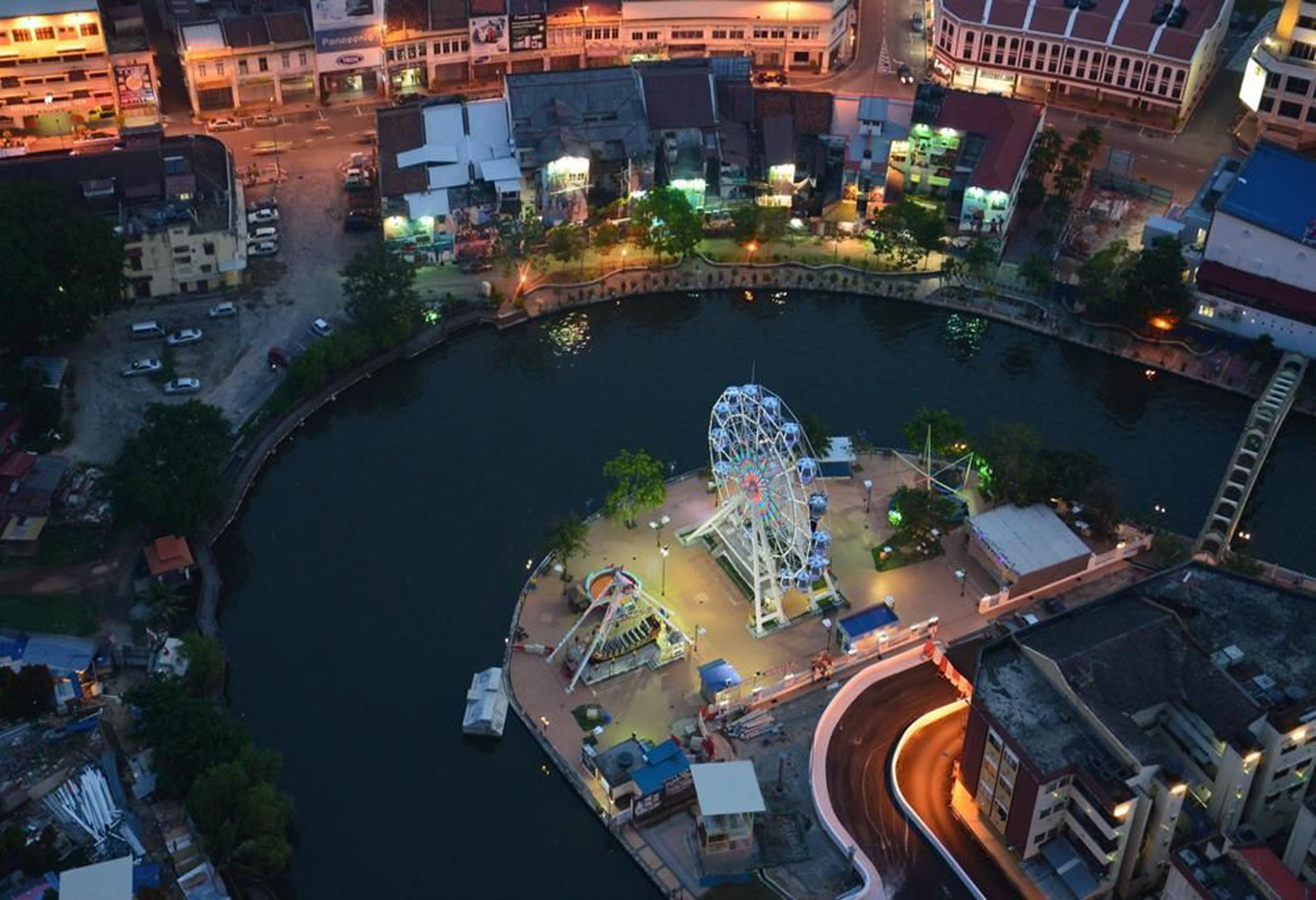 An aerial view of a waterfront amusement park with a Ferris wheel and various rides.