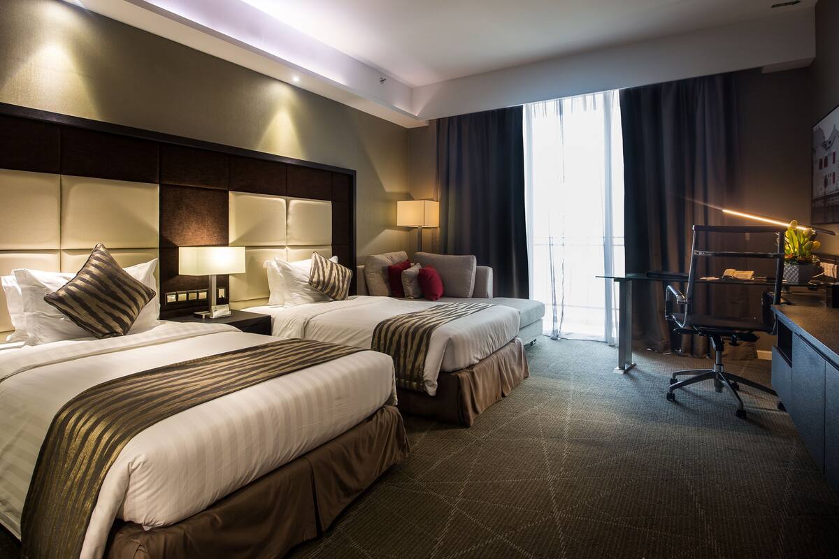 A hotel room with two beds, a desk, a chair, and a large window with curtains.