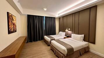 A hotel room with two beds, a wooden desk, a painting on the wall, and a large window with curtains.