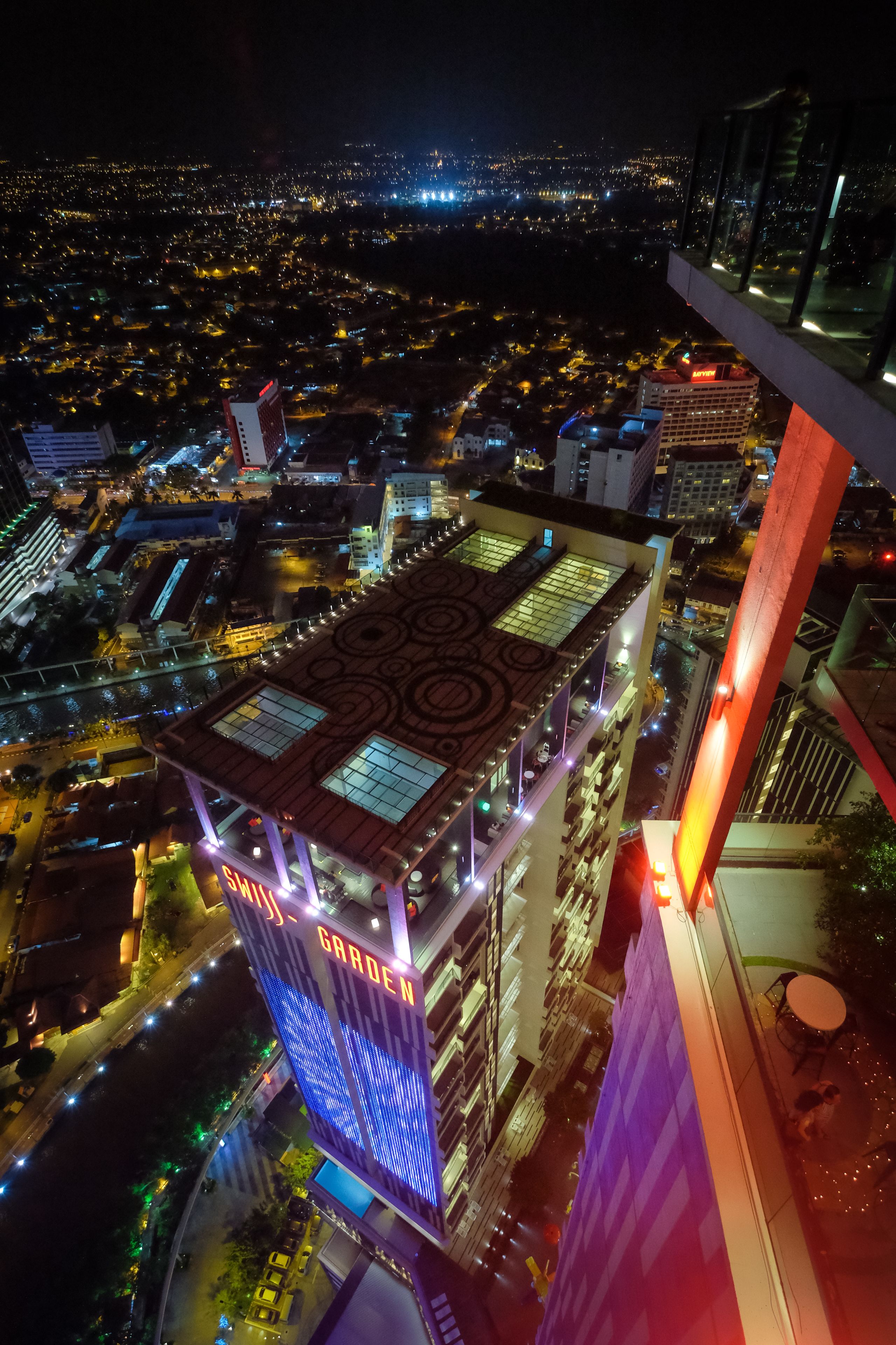 Un edificio de gran altura con jardín en la azotea y señalización iluminada.