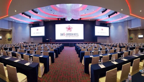 A conference room at the Swiss-Garden Hotel with multiple rows of tables and chairs, a large screen displaying the hotel's logo, and a carpeted floor.