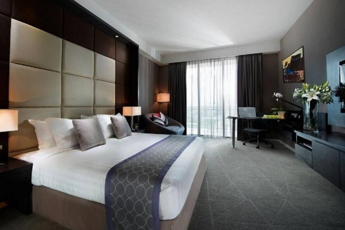 A hotel room with a large bed, a desk, a chair, a TV, and a balcony with curtains.