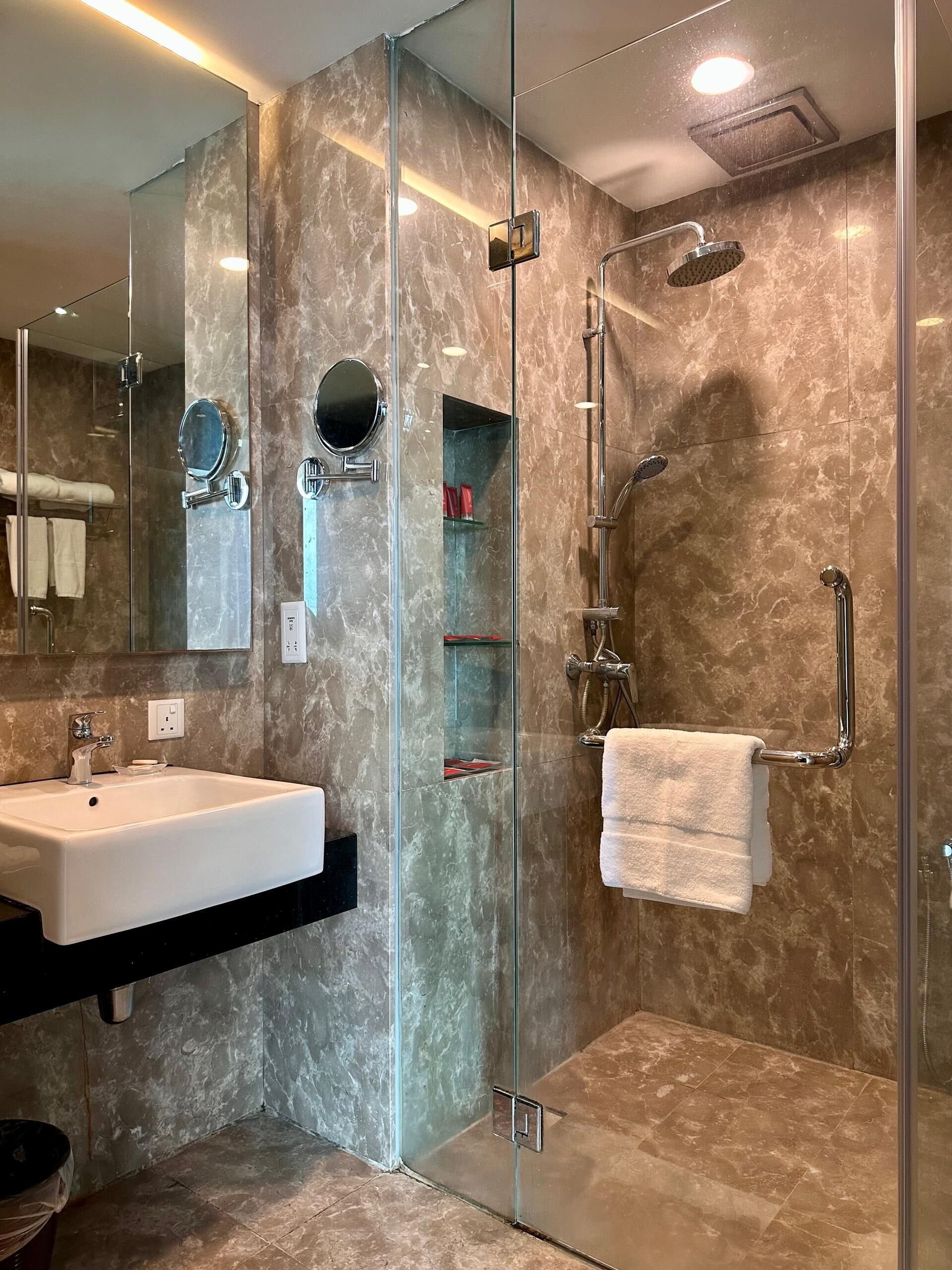 A modern bathroom with a glass-enclosed shower, a white sink, and a mirror.