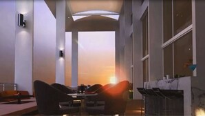 Un interior moderno con vistas al atardecer, una zona de estar con sillas y mesas, y un ventanal grande.