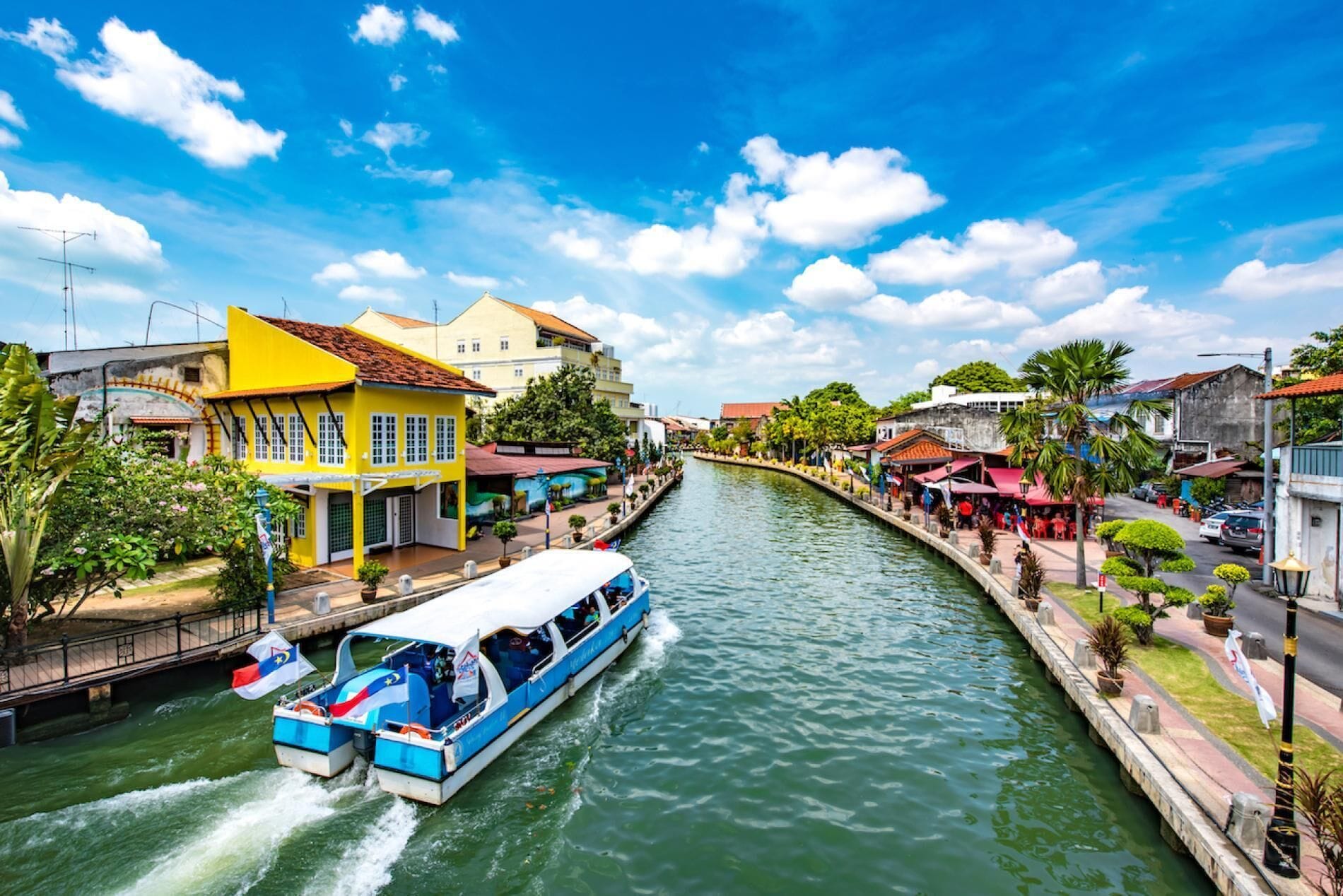 A narrow waterway flanked by buildings, a boat with a flag, and a clear sky.
