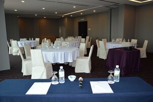 Sala de conferências com mesas redondas, cadeiras brancas e toalha de mesa azul.