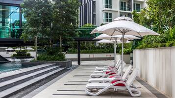 Un espace aménagé au bord de la piscine, avec des chaises longues et des parasols, une fontaine ou un autre élément décoratif aquatique, et un bâtiment moderne en arrière-plan.
