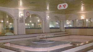 Una piscina con una fuente central, paredes azulejadas y un reloj en la pared.