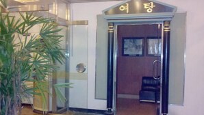 Entrada de hotel con puerta de cristal, un letrero encima y una planta a la izquierda.