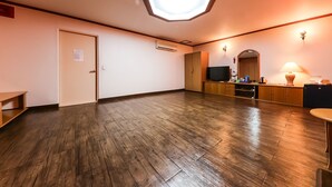 Una habitación amplia con piso de madera, una lámpara en el techo, una puerta y una pequeña cocina.