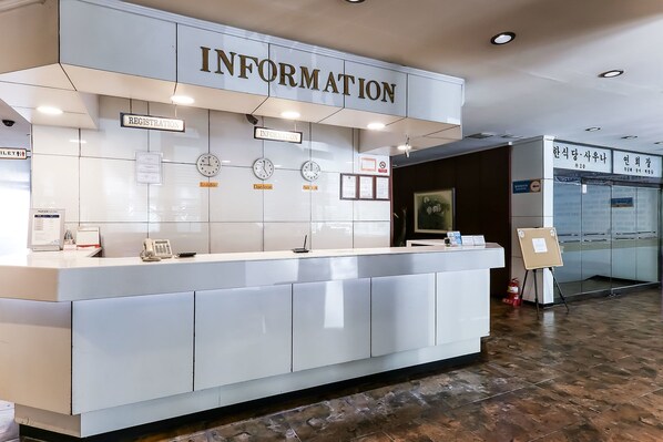 A reception desk with a sign reading "INFORMATION" above it. There are clocks on the wall, a phone, and a small sign indicating "Registration".