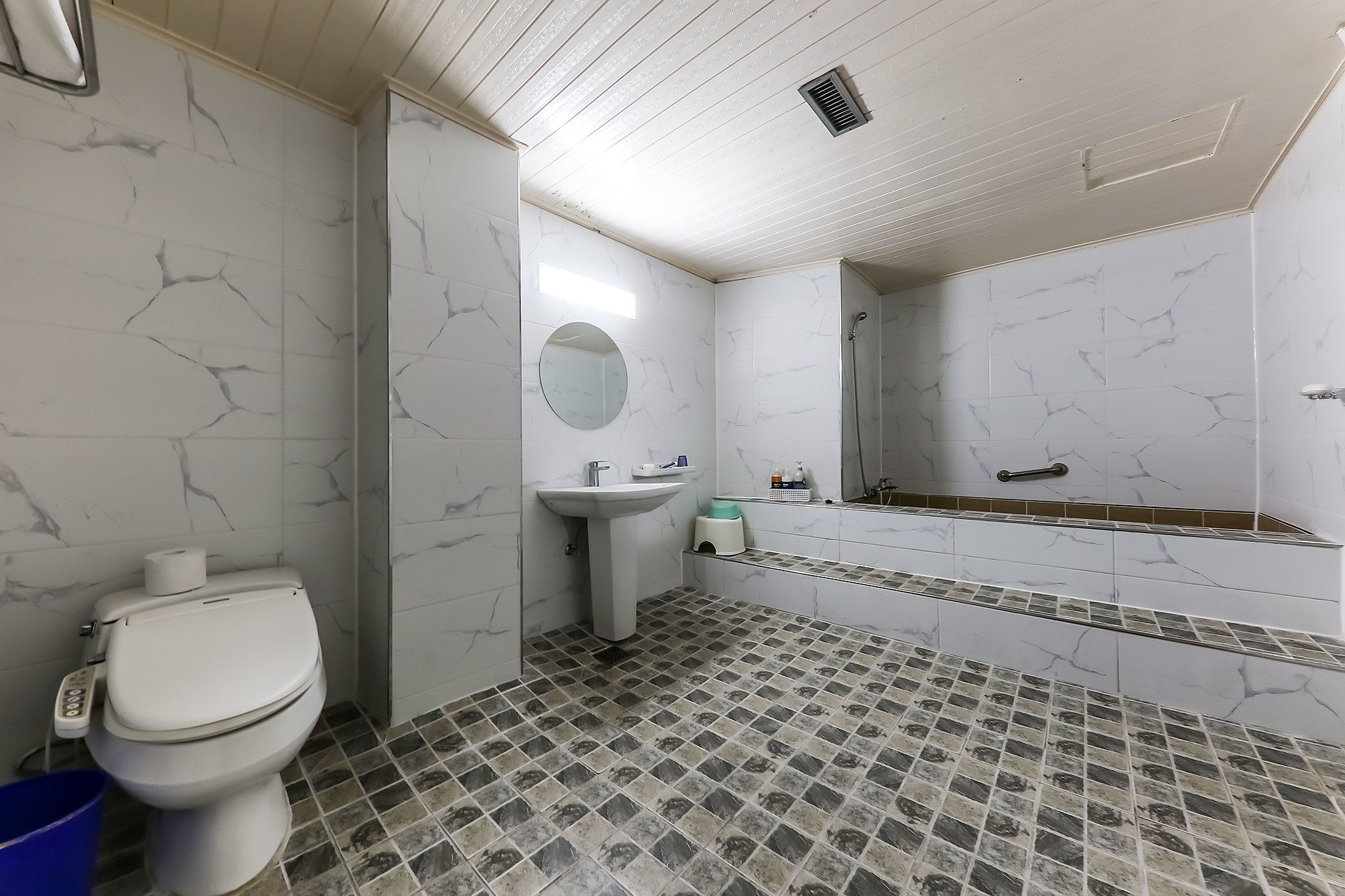 A bathroom with a toilet, sink, mirror, and shower.