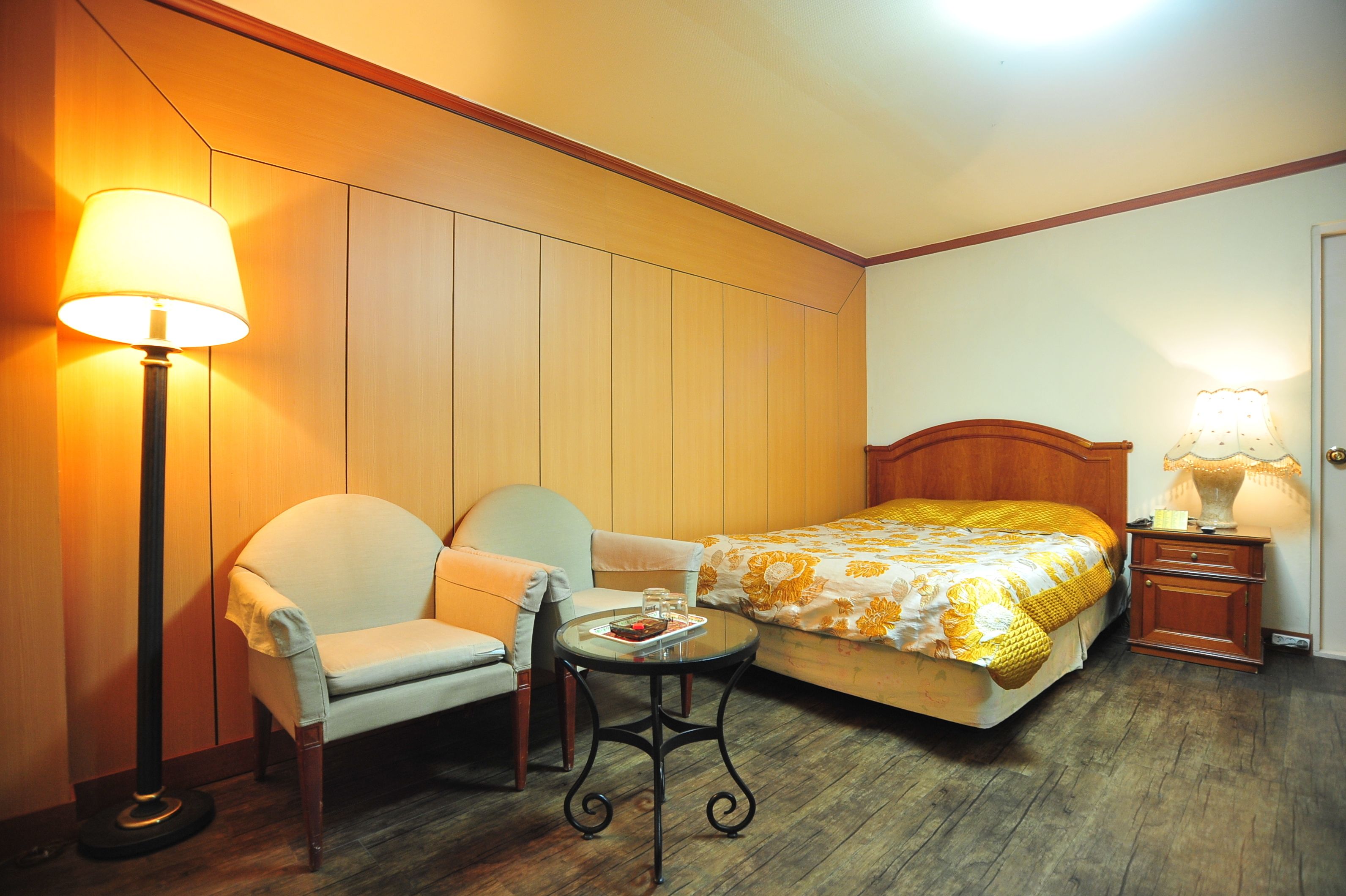 A hotel room with a bed, two chairs, a small table, and two lamps.