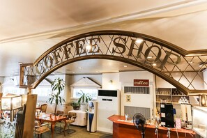 A coffee shop interior with a prominent sign reading "COFFEE SHOP," a reception desk, seating area, and a coffee machine.