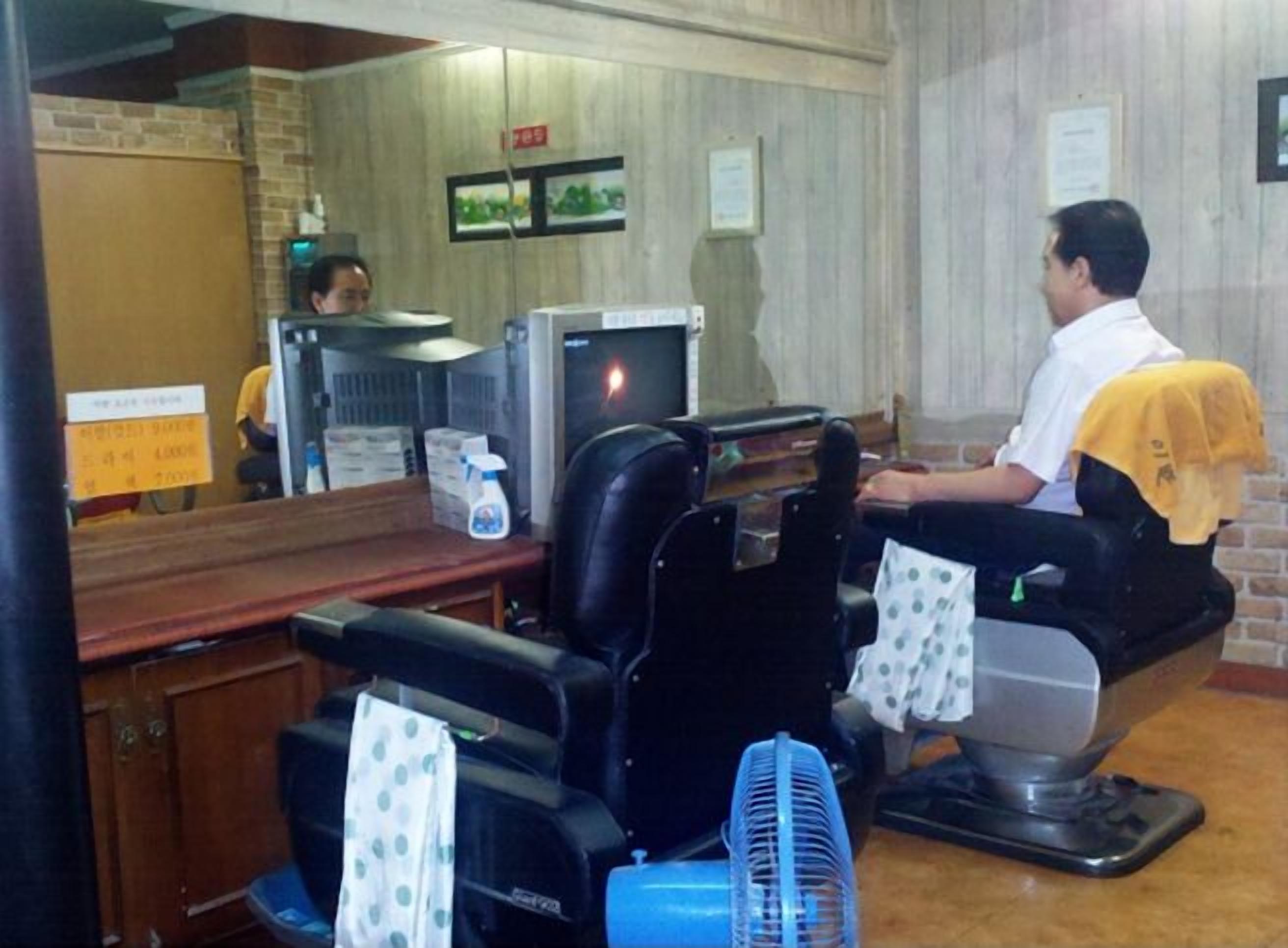 A barber shop with a mirror, a television, and a few chairs.