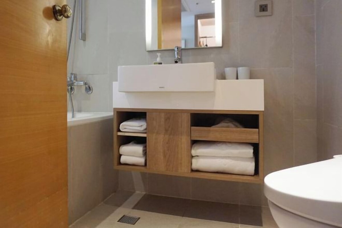 A modern bathroom with a white sink, wooden vanity, and a bathtub.