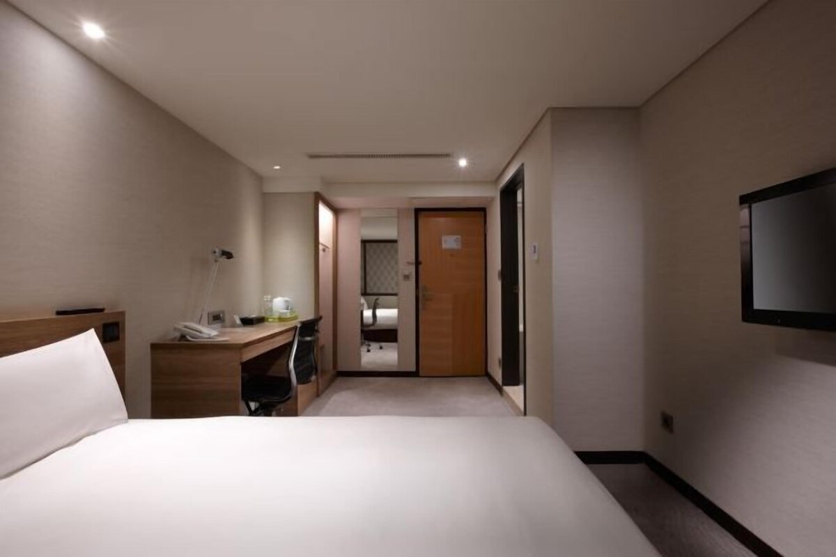 A hotel room with a bed, desk, chair, and a TV mounted on the wall.