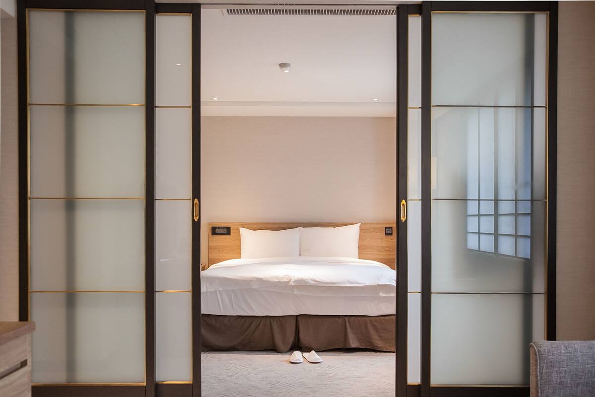 Et hotelværelse med en seng, et trægavl og en skydedør med frostet glas.