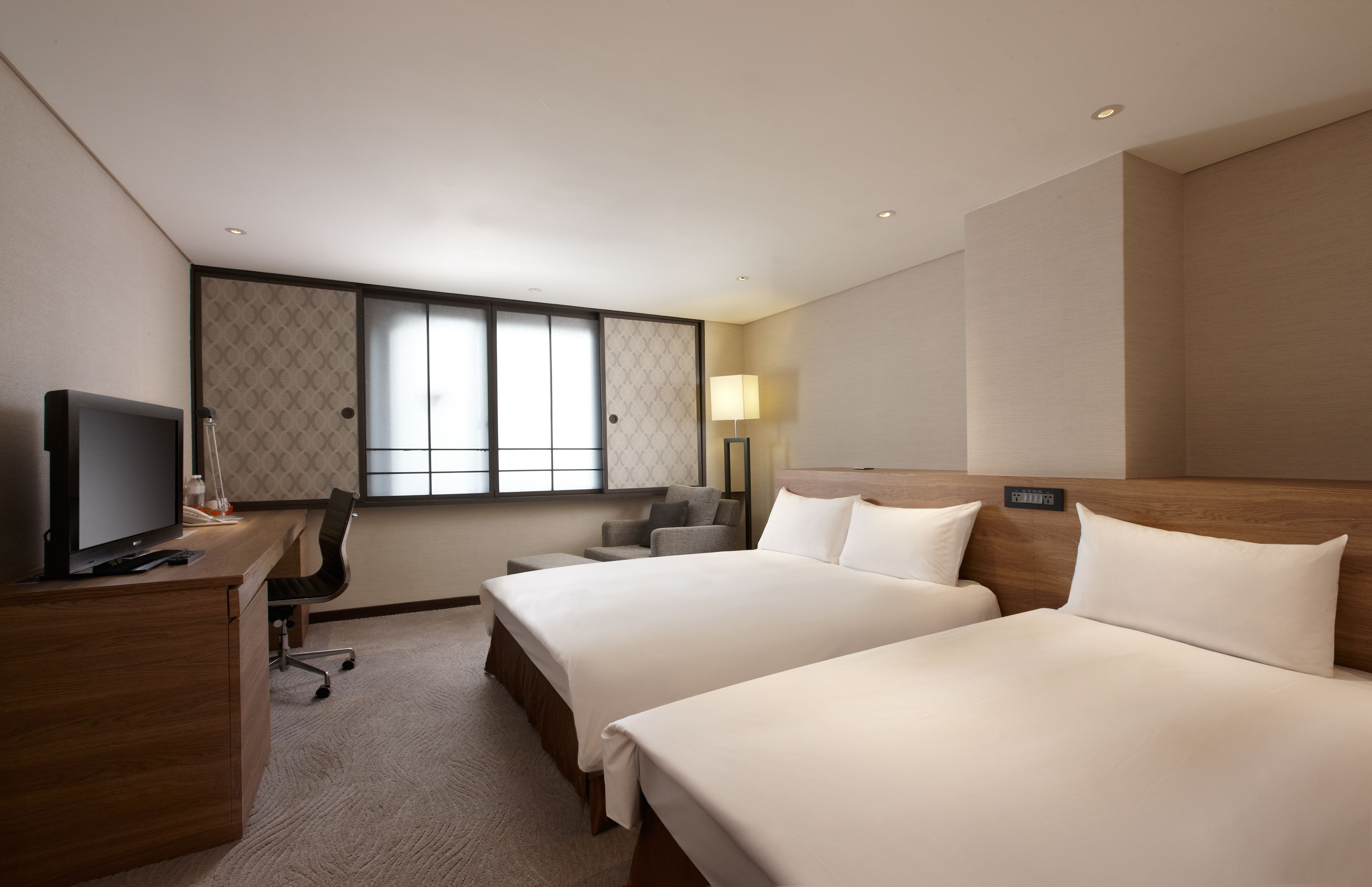 A hotel room with two beds, a desk with a TV, a chair, and a window with a view.