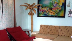 A living room with a sofa, a red chair, a tall plant, and a framed floral painting on the wall. - Baan Rim Lay Lipa Noi (Koh Samui)