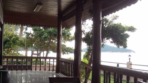 An outdoor covered seating area with wooden tables and chairs, a railing, and a view of a body of water and trees. - Baan Rim Lay Lipa Noi (Koh Samui)