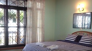 A hotel room with a large bed, a round table, a window with a view, and a wall-mounted light fixture. - Baan Rim Lay Lipa Noi (Koh Samui)