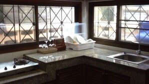 A kitchen with dark wooden cabinets, a granite countertop, a sink, and a window with a view of the outside. - Baan Rim Lay Lipa Noi (Koh Samui)