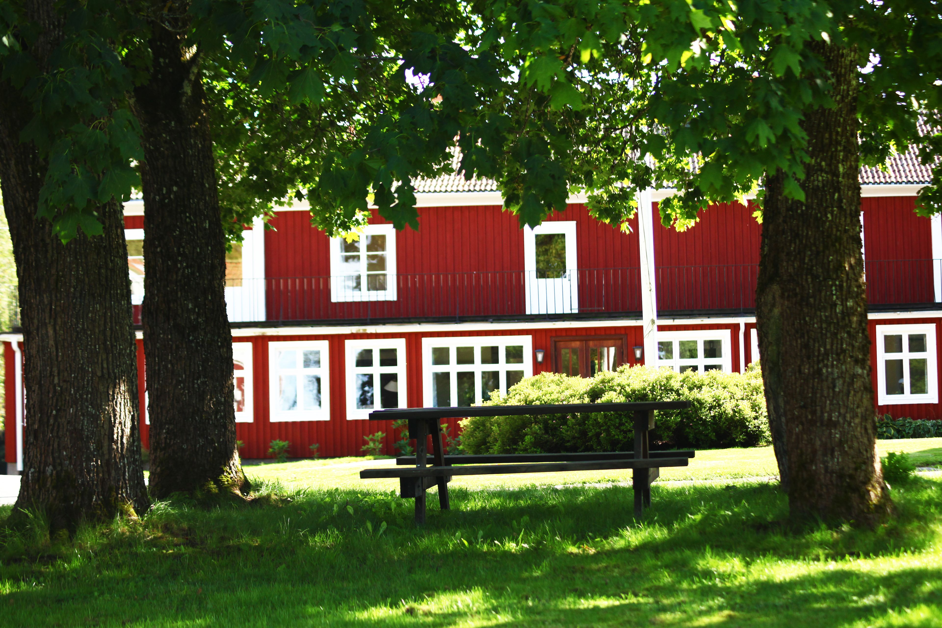 A red building with white trim, a bench, and trees in a grassy area.
