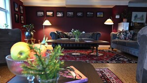 A living room with a dark red wall, a sofa, a coffee table, and a patterned rug. - Nyhyttans Kurort (Nora)