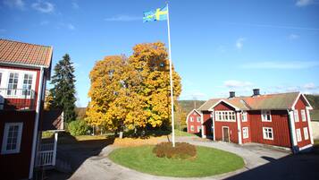 Un bâtiment rouge surmonté d’un mât portant un drapeau, un grand arbre aux feuilles jaunes et un ciel bleu dégagé.
