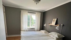 A bedroom with a bed, a window with curtains, a bedside table, and a wall-mounted lamp. - Nyhyttans Kurort (Nora)