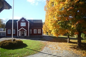 A red building with a white door and windows, surrounded by a lawn and trees with yellow leaves. - Nyhyttans Kurort (Nora)
