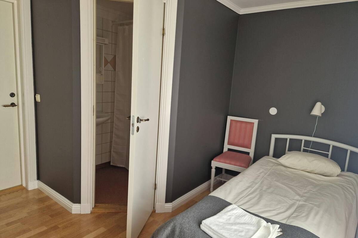 A bedroom with a bed, a chair, a bedside table, and a door leading to a bathroom.