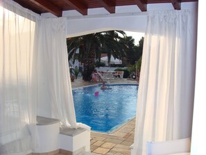 A pool area with a clear view of the water, steps leading to the pool, and a covered seating area with umbrellas. - Villa Christina (Skiathos)