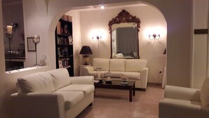 A living room with a white sofa, a coffee table, and a bookshelf. - Villa Christina (Skiathos)