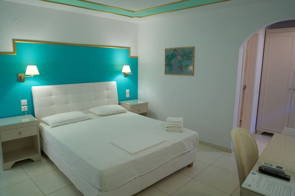 A hotel room with a large bed, two bedside tables with lamps, a chair, and a desk with a remote control.