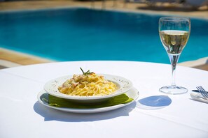 A dining table with a plate of pasta, a glass of white wine, and cutlery. - Villa Christina (Skiathos)