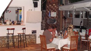 A restaurant with outdoor seating, a bar area, and a stone wall. - Villa Christina (Skiathos)